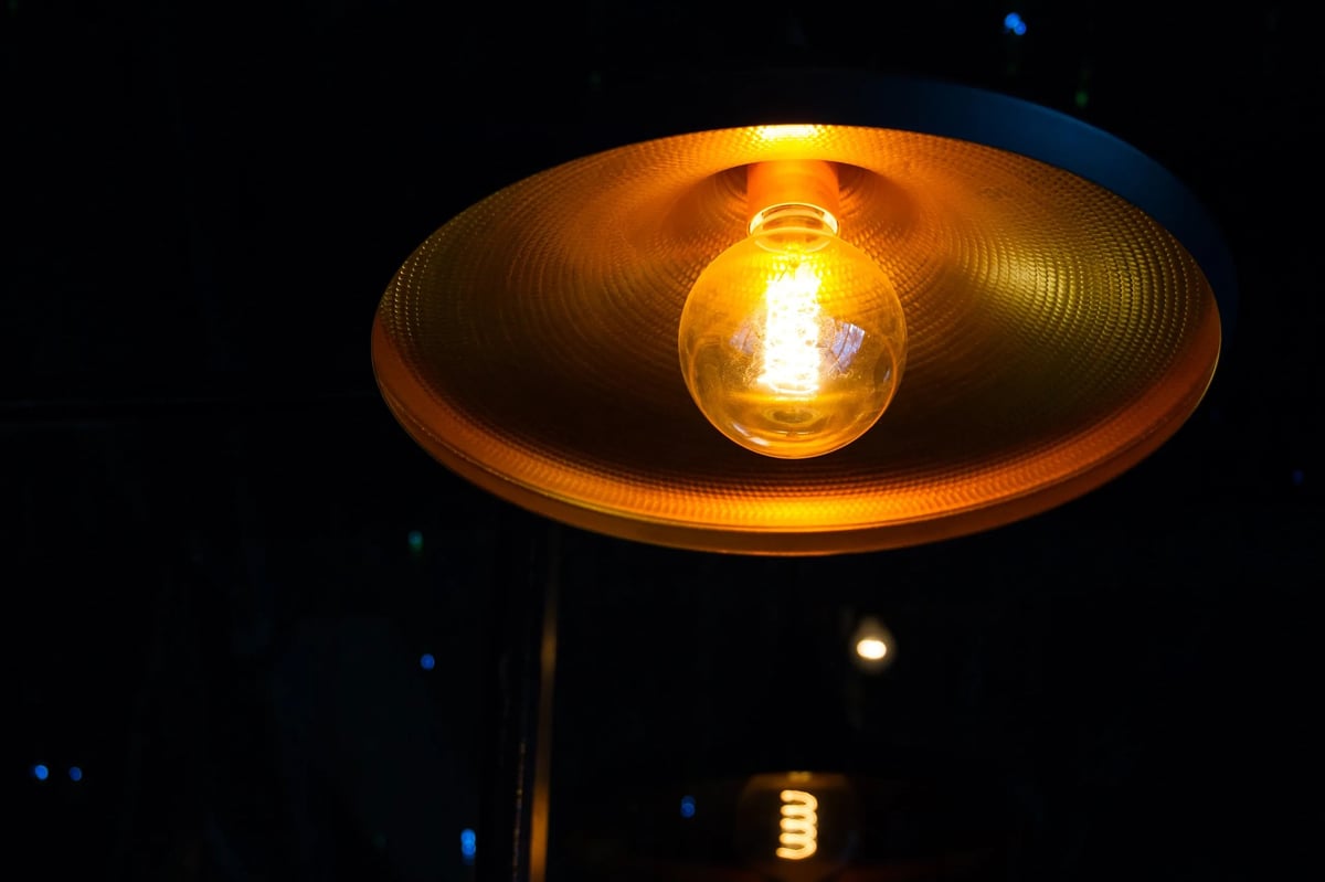 Glowing incandescent bulb suspended inside a large metallic dish lamp at DOMUS at night