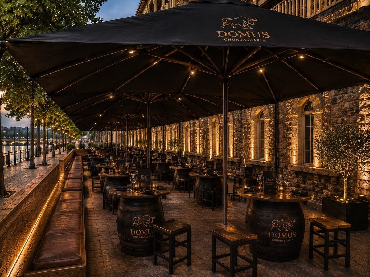 Evening outdoor dining terrace with black Domus umbrellas, wooden chairs, and stone building facade with warm lighting